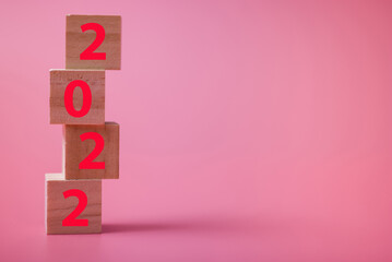 Happy New Year. Wooden cube with the number 2022 on a pink background