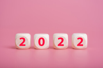 Happy New Year. Wooden cube with the number 2022 on a pink background