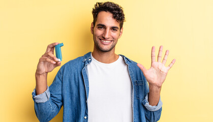 hispanic handsome man smiling and looking friendly, showing number five. asthma concept