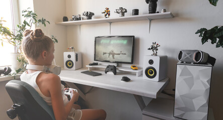 Girl holding white wireless gamepad against white computer dream desk.