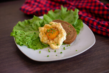 Fried egg on a white plate with leaves of salad and bread, brown table and red textile