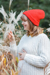 Beautiful young pregnant woman in a knitted sweater, hat near the pampas grass. walks in the autumn...