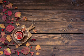 Autumn background with copy space. Tea with lemon, leaves and berries on a wooden table.
