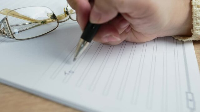 close-up female hand writes with a pen on paper the words of will, the concept of a legal order on her movable and immovable property in the event of a person's death for the heirs