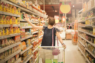 Beautiful Asian woman wearing a facemask shopping in the supermarket at the Grocery shelf. This is a new normal shopping  after coronavirus or post covid-19 outbreak pandemic.