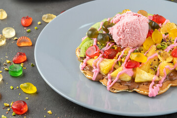 Heart waffle with kiwi and pineapple with gummy candy and ice cream on it.