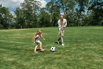 Active young father playing football together with his little daughter on the grass field in the...