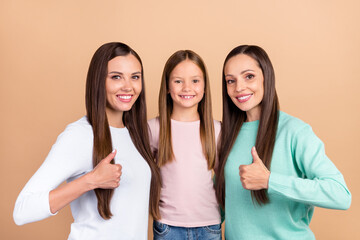Portrait of three beautiful trendy cheerful girls hugging showing thumbup trust isolated over beige pastel color background