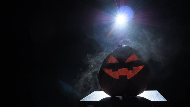 Halloween pumpkin smile and scary eyes for a party surrounded by smoke .scary pumpkin, Jack O Lantern for Halloween with eyes glowing inside on a black background.