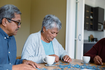 Two diverse female and male friends sitting at table and doing puzzles
