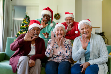 Group of happy diverse group of senior friends in santa hats having video call at christmas time