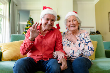 Happy caucasian senior couple in santa hats having video call at christmas time