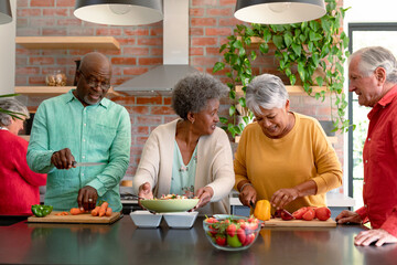 Group of happy diverse senior male and female friends cooking together at home