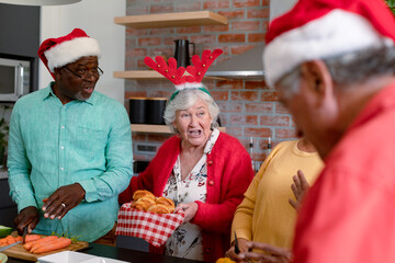 Three diverse senior male and female friends in christmas hats cooking together in kitchen