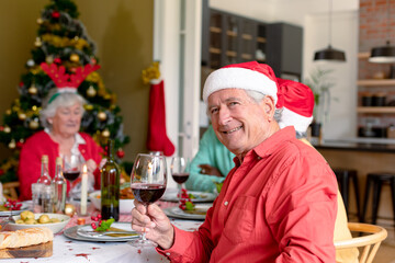 Happy caucasian senior man holding glass of vine at christmas table