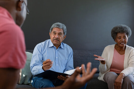Mixed race senior male counsellor with clipboard advising diverse group of senior friends