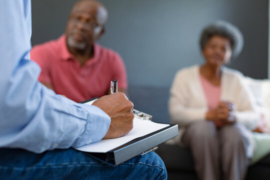 Hand of mixed race senior male counsellor iwth clipboard advising diverse group of senior friends