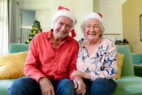 Happy caucasian senior couple in santa hats having video call at christmas time