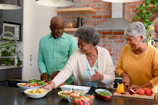 Group of happy diverse senior male and female friends cooking together at home