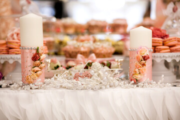 Delicious desserts at the wedding candy bar in the buffet area: candles decorated with rosebuds and ribbons