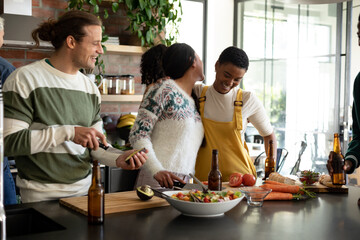 Group of happy diverse female and male friends drinking beer and cooking together in kitchen