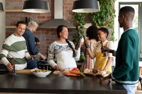 Group of happy diverse female and male friends drinking beer and cooking together in kitchen