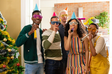 Group of happy diverse female and male friends with whistles and colorful hats celebrating new year