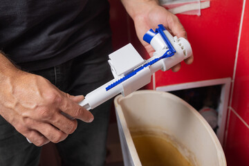 Toilet tank parts replacement. A man in orange gloves repairs the toilet tank drain.