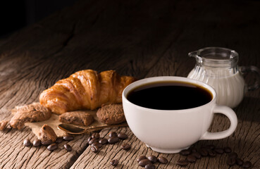 Coffee cup with croissant, bread, bakery or breakfast cake laying on a wooden table on a black needle background