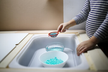 Child plays in the Sensory hydrogel box, children's hands touch, roll and play with blue water beads, Sensory development and Montessori, themed activities with children
