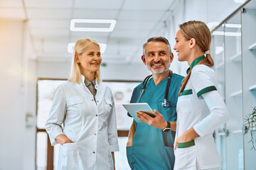 Three healthcare workers stand using tablet computer together in a hallway in the hospital.