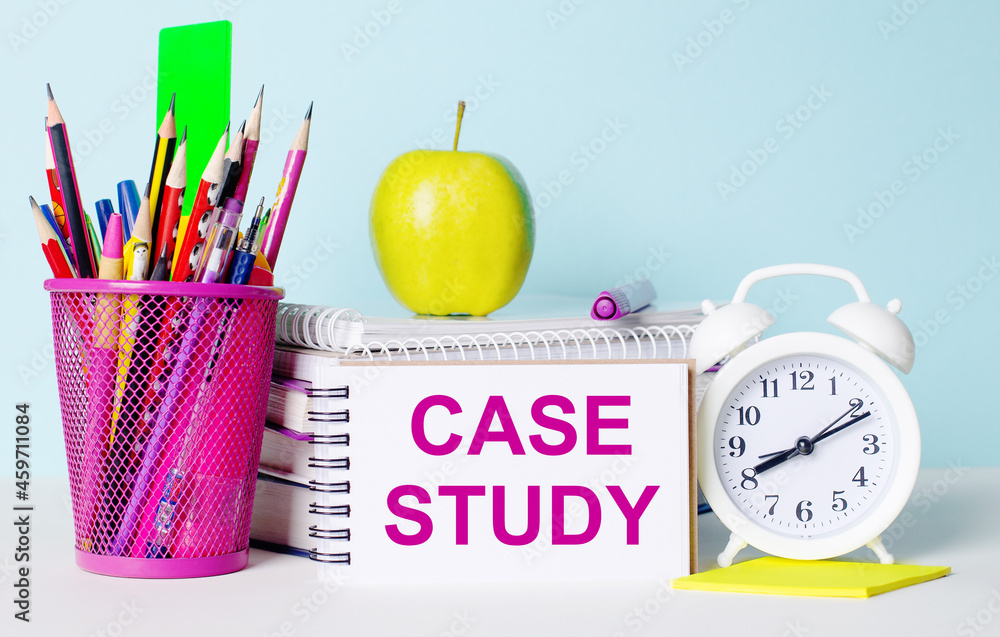 Poster on a light table there are books, stationery, a white alarm clock, an apple. next to it is a noteboo
