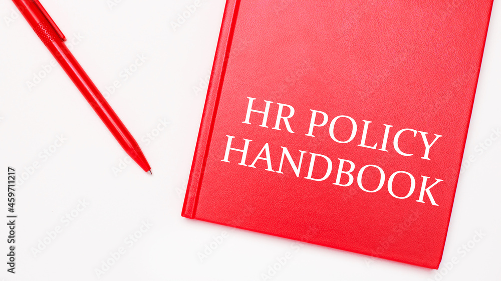 Poster the text hr policy handbook is written on a red notepad near a red pen on a white table in the offic