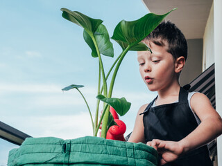 Content boy with watering can and blooming plant on balcony