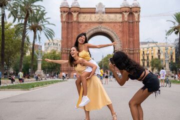 Cheerful women taking photo on city square - obrazy, fototapety, plakaty