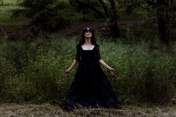 Witch in black dress in dark forest