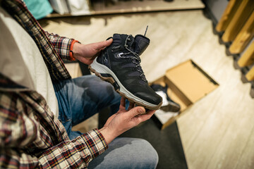Caucasian man chooses and measures hiking boots at a sports and travel store. Man looking at hiking...