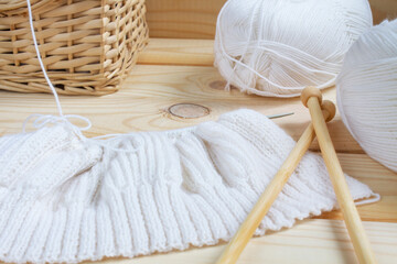 Fototapeta na wymiar Cozy home atmosphere. Women's hobby is knitting. The beginning of the process of knitting a women's sweater from white yarn. Natural materials. Knitting concept