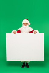 Santa claus holding placard with copy space and looking at camera on green background