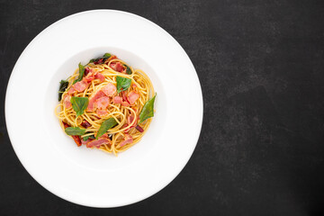 top view shot of Spaghetti Pasta with Dried Chilli, Garlic, Sweet Basil and Bacon in white ceramic plate on dark tone texture background