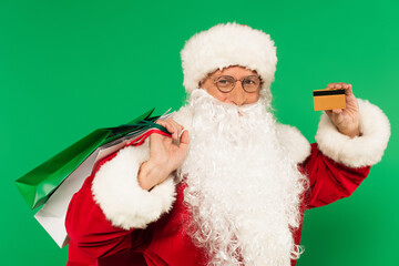 Santa claus with shopping bags and credit card looking at camera isolated on green