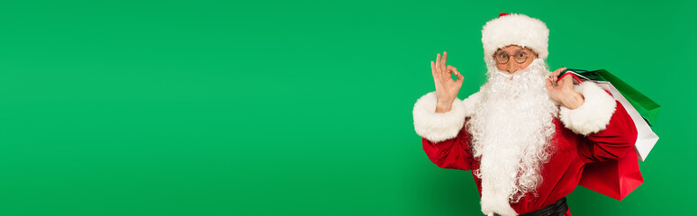 Bearded santa claus with shopping bags showing ok gesture isolated on green, banner