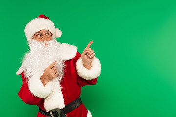 Santa claus in hat and costume pointing with fingers isolated on green