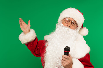 Santa claus with microphone pointing with hand isolated on green