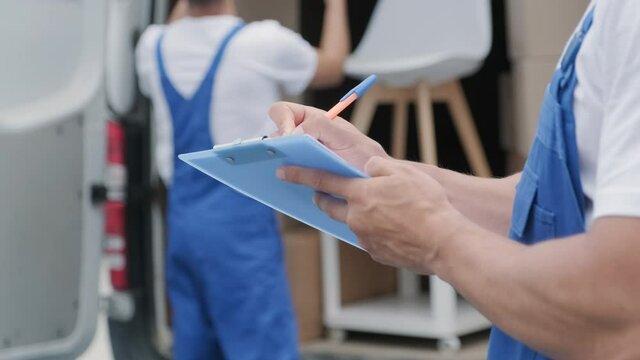 Two young workers of removal company are loading boxes and furniture into a minibus