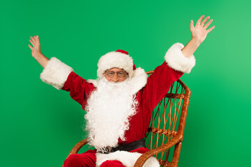 Excited santa claus sitting on rocking chair isolated on green
