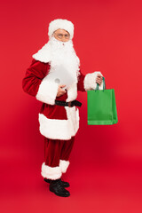 Father christmas holding laptop and shopping bags on red background