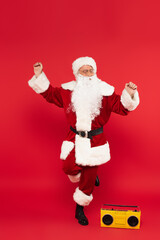 Fototapeta na wymiar Santa claus dancing near boombox on red background