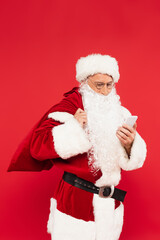 Santa claus with sack using mobile phone isolated on red
