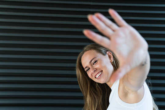 Cheerful businesswoman showing palm in front of black wall